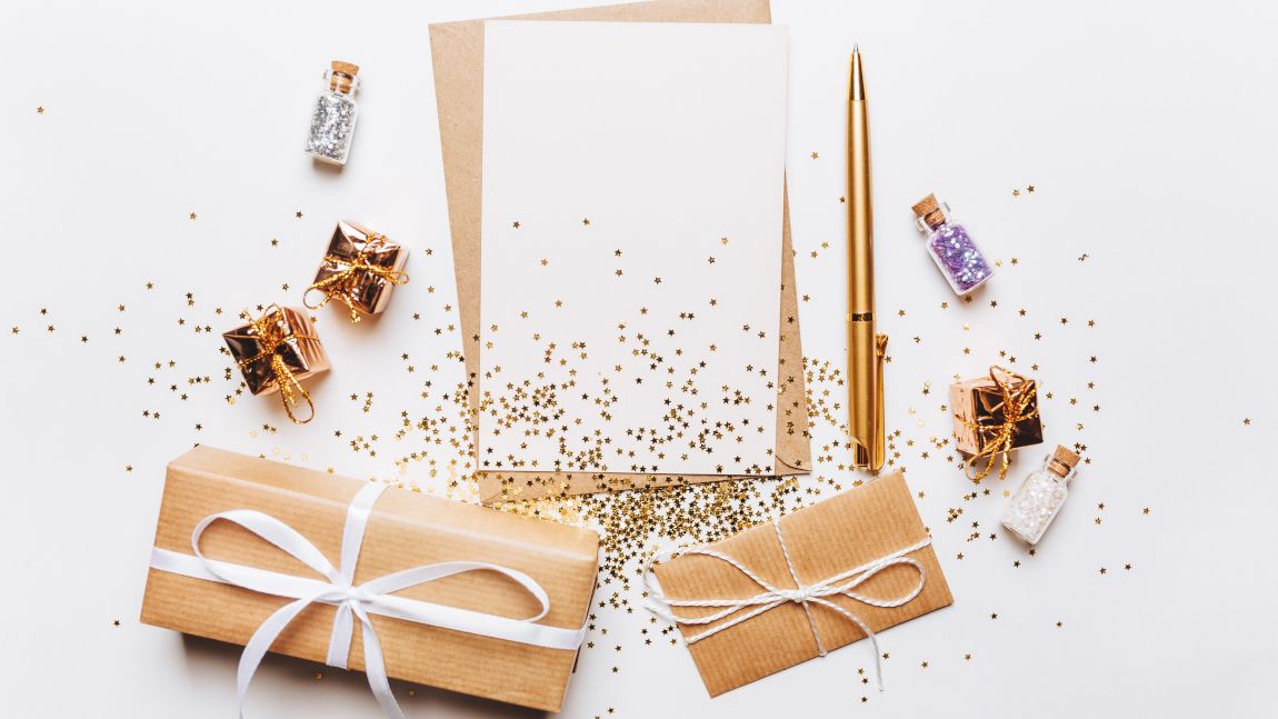 5 kleine Pakete, drei Flaschen mit Konfetti, Briefpapier und Stift umgeben von goldenem Konfetti